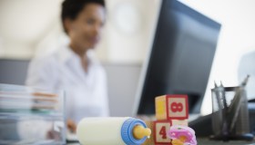 Baby bottle and blocks on African American woman's desk