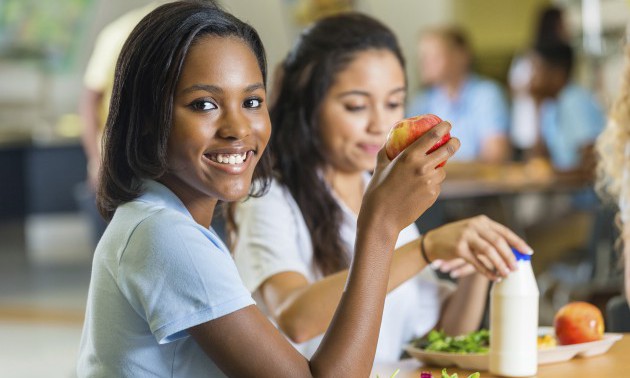 Teenager eating healthy lunch with friends in school lunchroom
