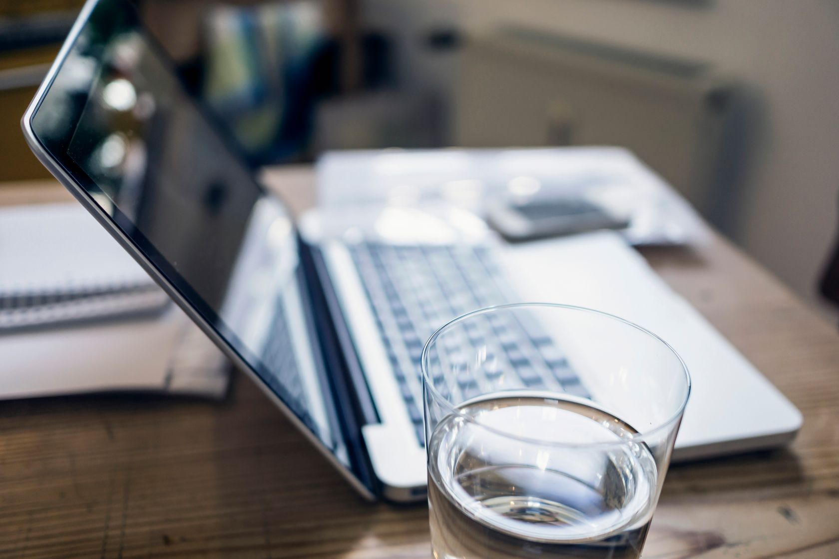 Glass of water, documents and laptop on a wooden table