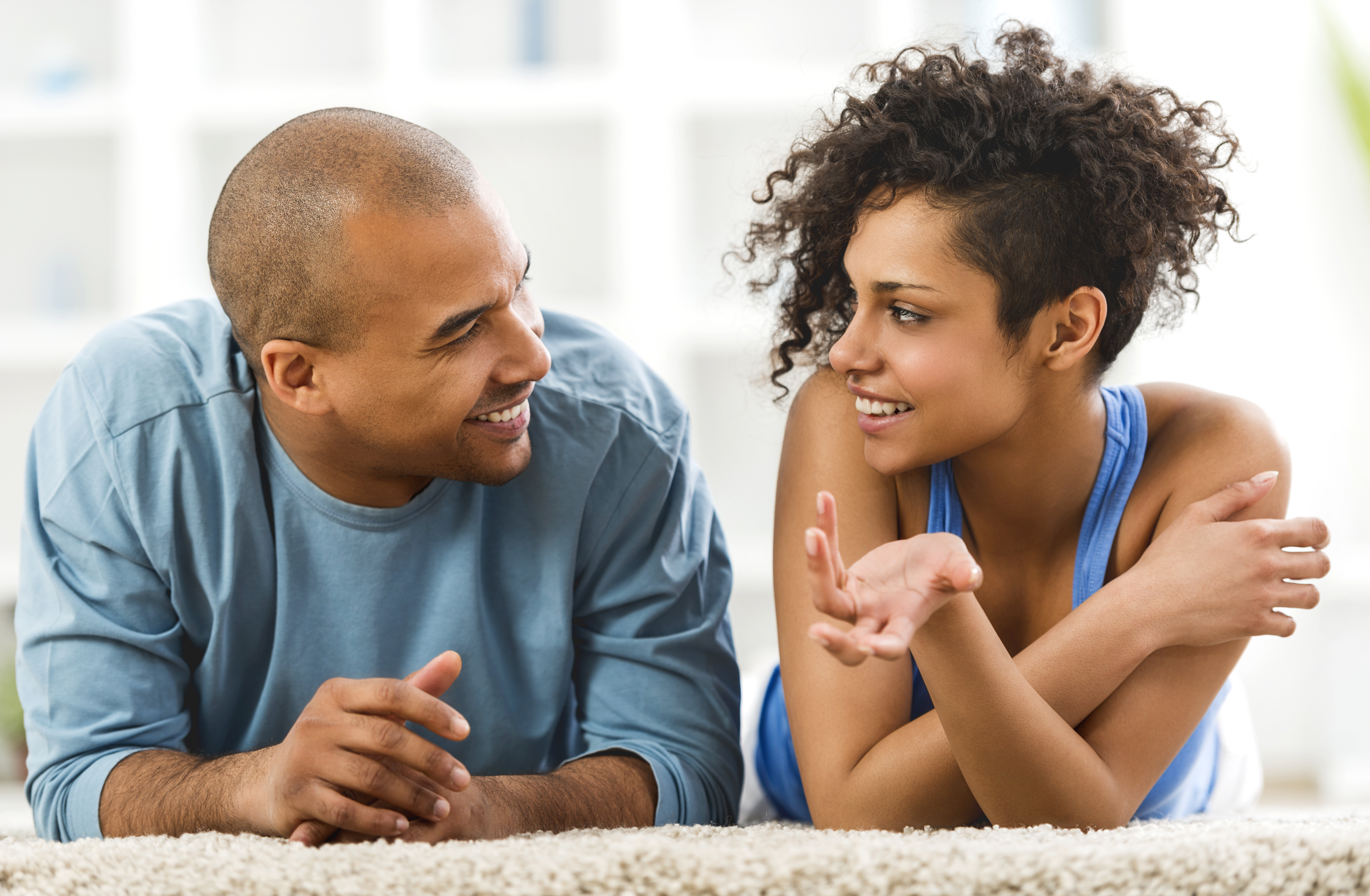 Smiling African American couple lying on carpet and communicating.
