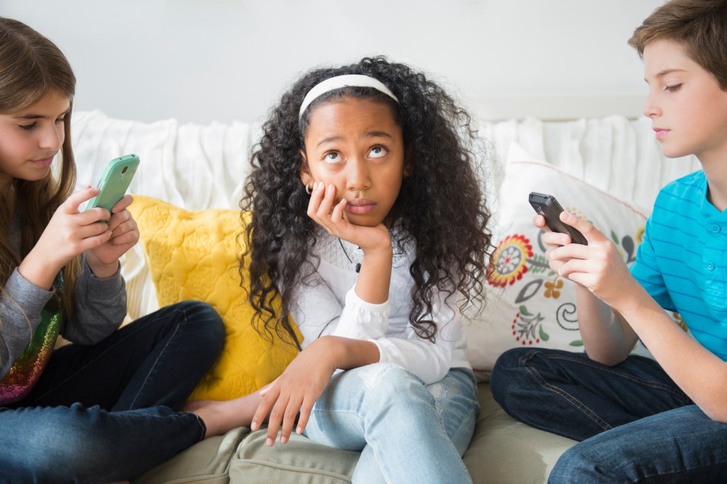 Annoyed girl ignoring friends using cell phones on sofa