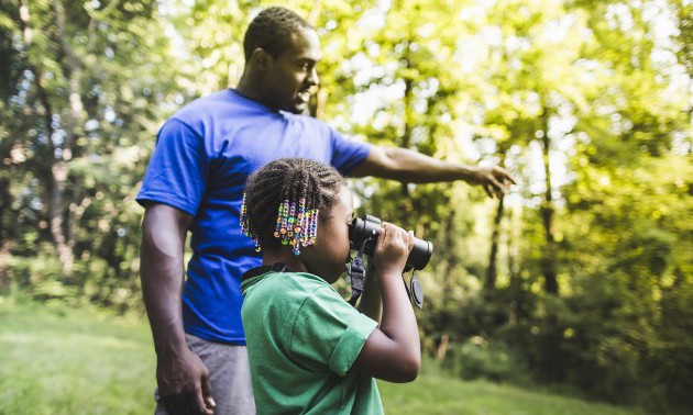 Father and daughter watching with binoculars in forest eco camp