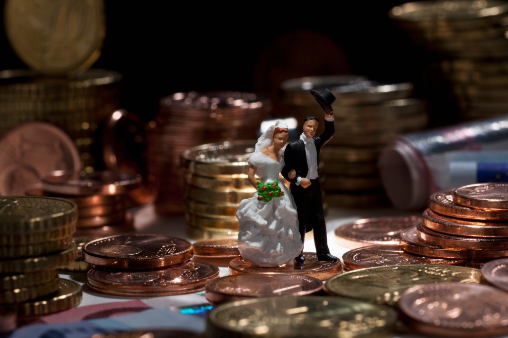 Miniature wedding couple figurines amidst stacks of European Union coins