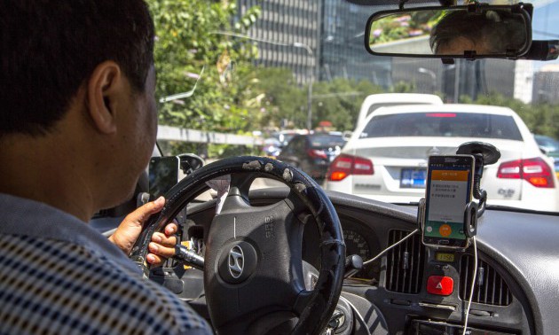 A taxi driver is using Didi Dacha App while driving on the...