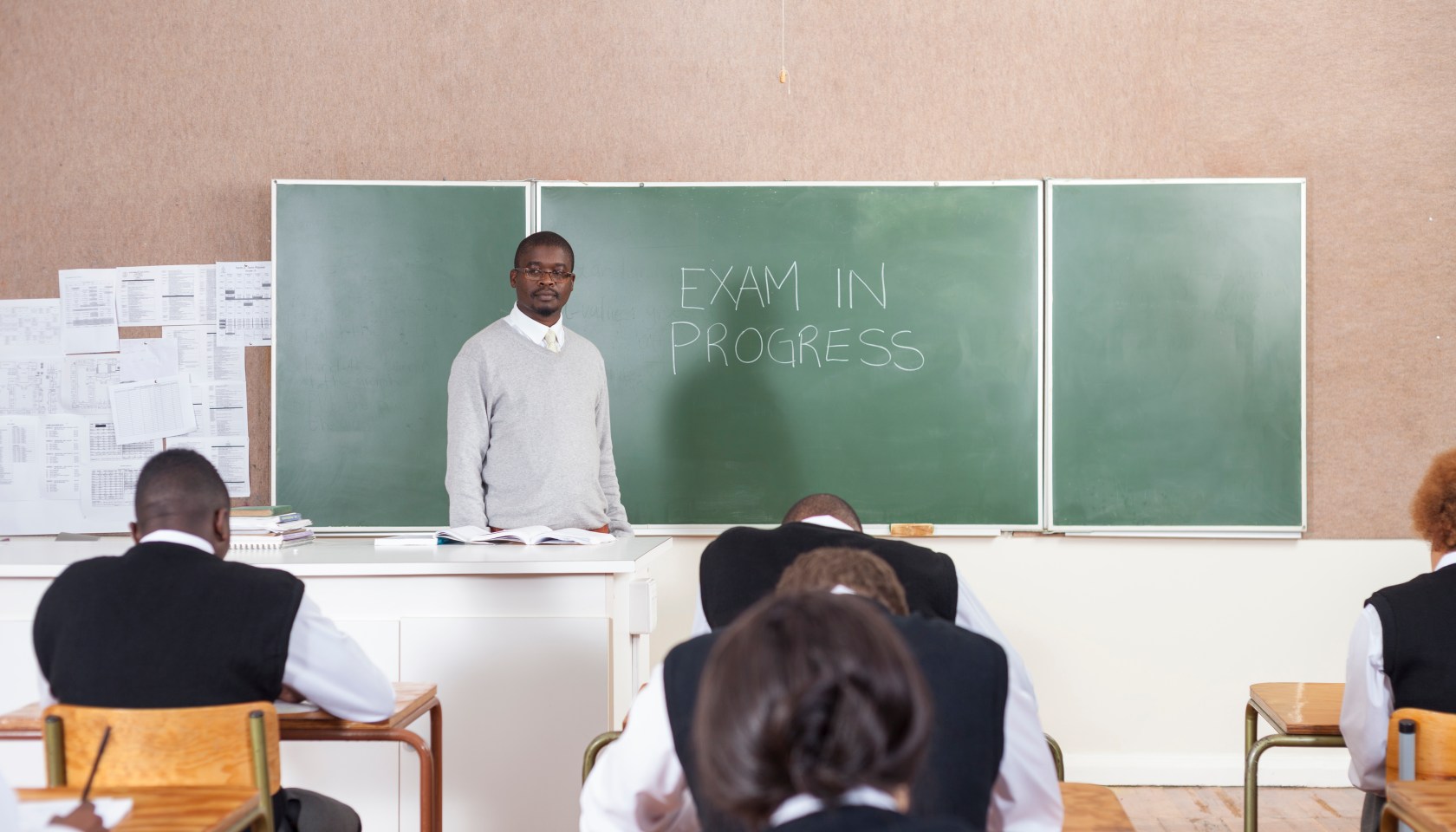 A Teacher standing by the chalk board while students write an exam. Cape Town, South Africa