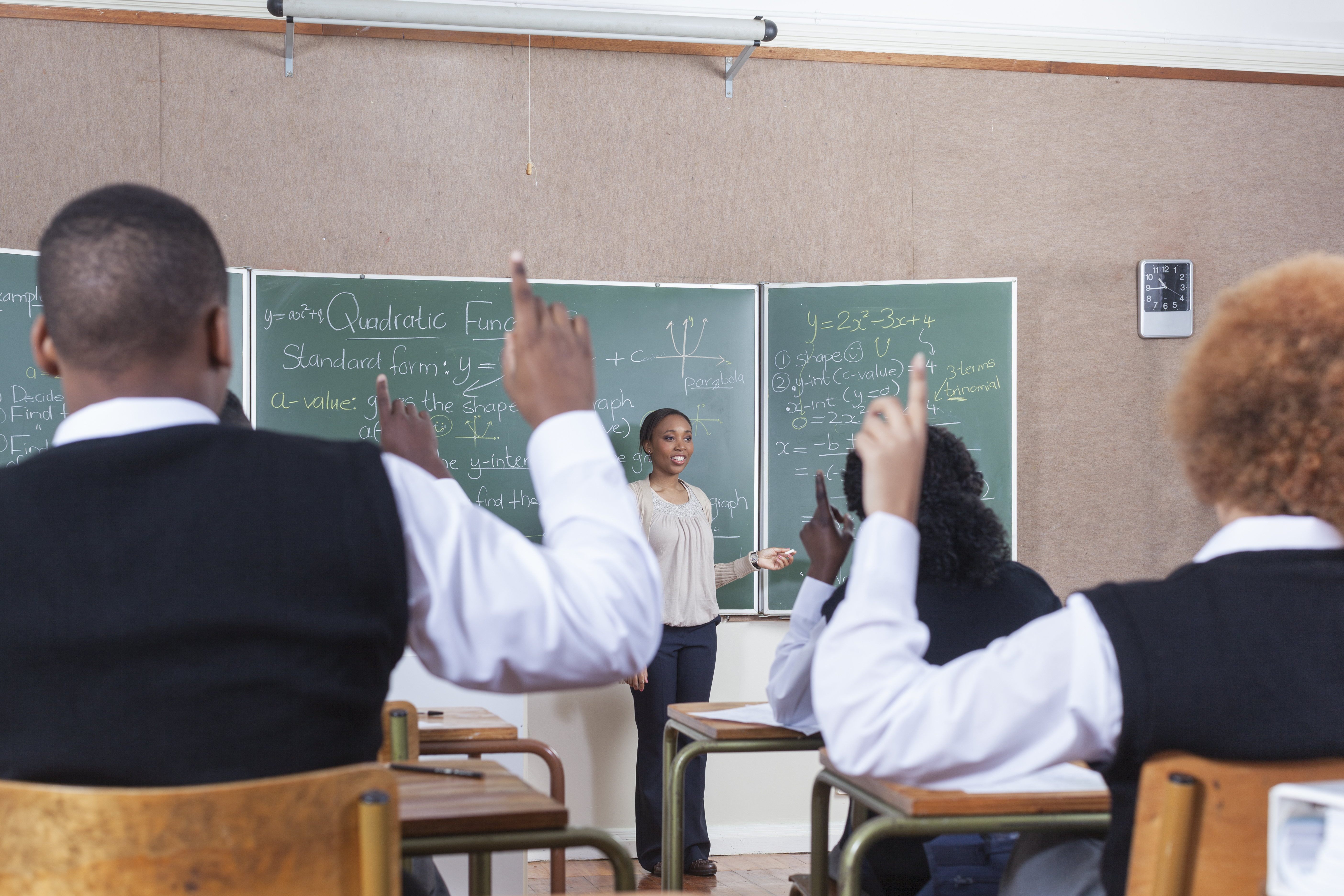 Medium POV of the back of students with their hands raised in classroom, Cape Town, South Africa