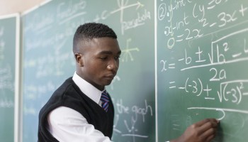 Medium shot of African male student writing on chalkboard, Cape Town, South Africa