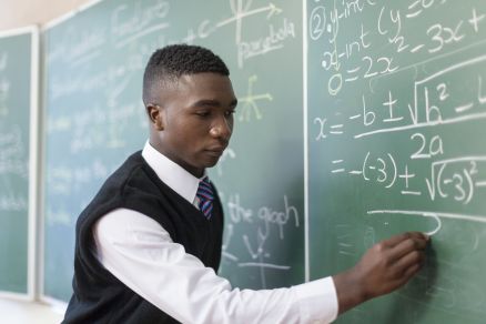 Medium shot of African male student writing on chalkboard, Cape Town, South Africa