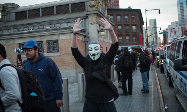 A participant in the rally wearing a Guy Fawkes mask raises...