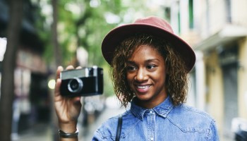 Portrait of smiling young woman wearing hat and denim shirt holding camera
