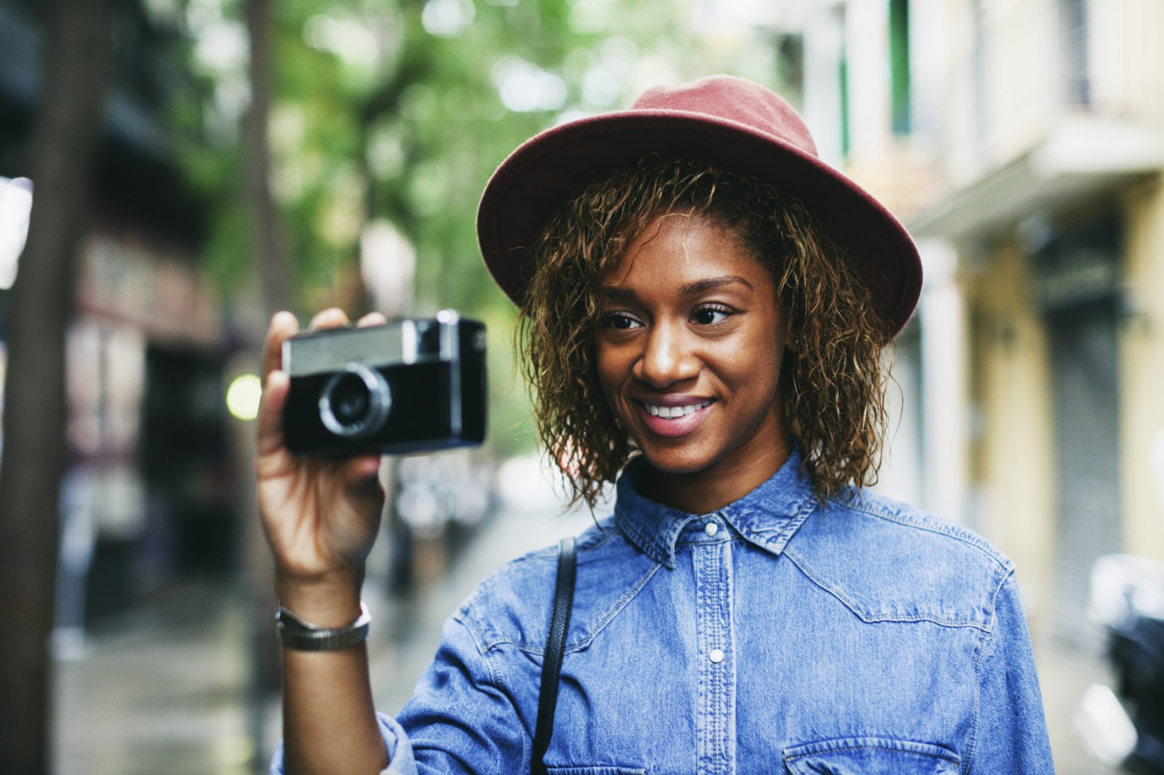 Portrait of smiling young woman wearing hat and denim shirt holding camera