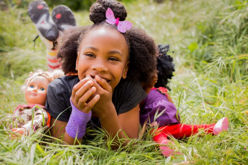 Black girl playing with dolls in tall grass