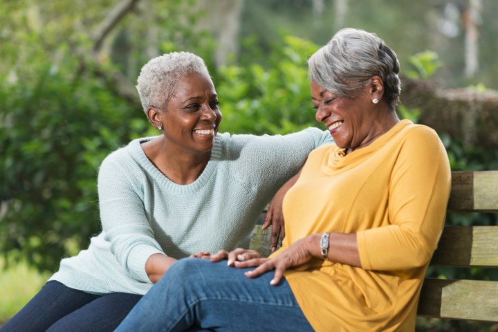 Two senior women sitting on park bench laughing