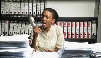 Female office worker at desk screaming into telephone receiver