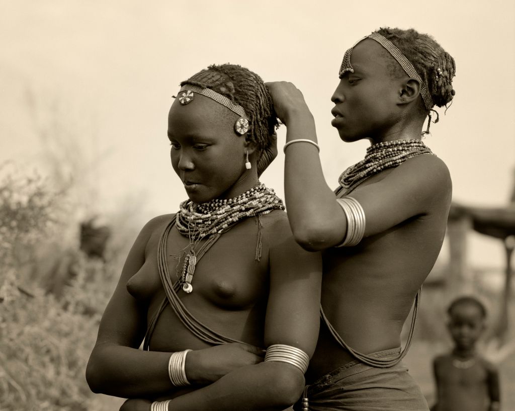 Ethiopia, Omo Delta. A Dassanech girl braids her sister's hair at her village in the Omo Delta