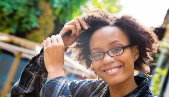 Confident happy young black woman arranging her hair outdoors