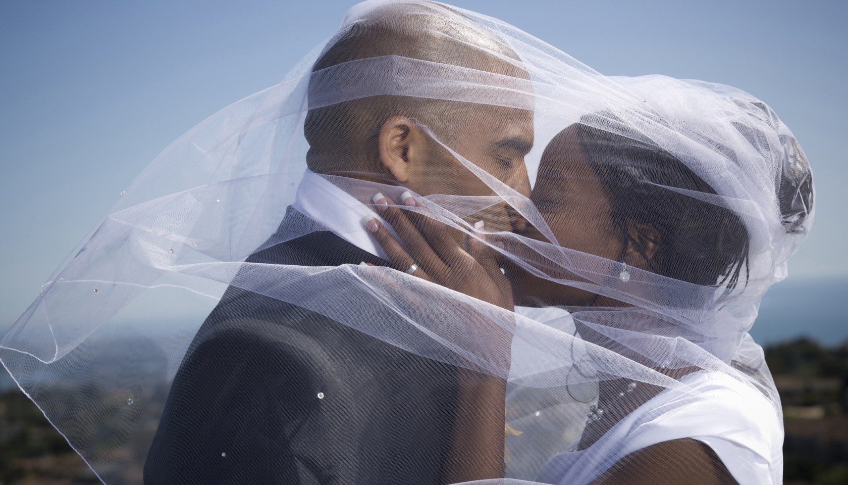 Profile of a newlywed couple kissing each other under a veil
