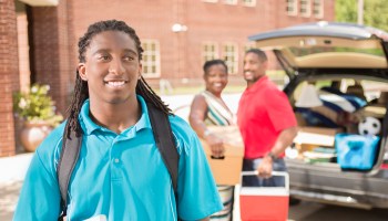 African-descent boy moves into college. Packed car, family. School campus.