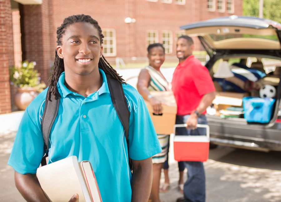 African-descent boy moves into college. Packed car, family. School campus.