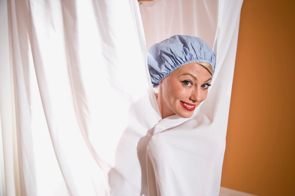 Woman in shower cap peeking out from behind curtain
