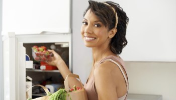 A healthy young woman putting a container of fresh strawberries into the fridge