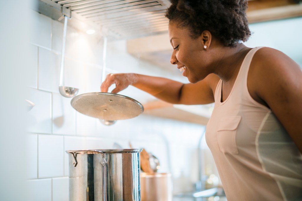 Young pretty black woman make soup in kitchen