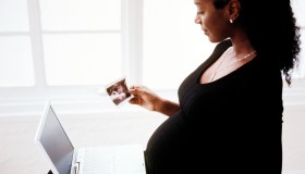 side profile of a pregnant woman sitting with a laptop computer and a photograph