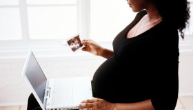 side profile of a pregnant woman sitting with a laptop computer and a photograph