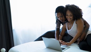 Lesbian couple sitting on bed, looking at laptop