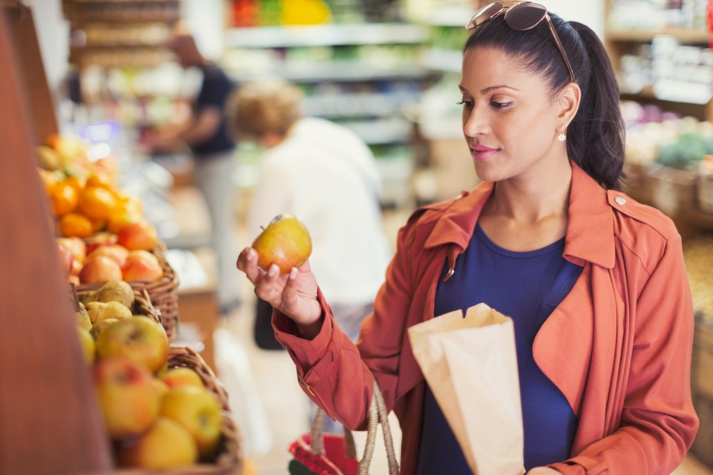 Woman shopping, examining apple in grocery store