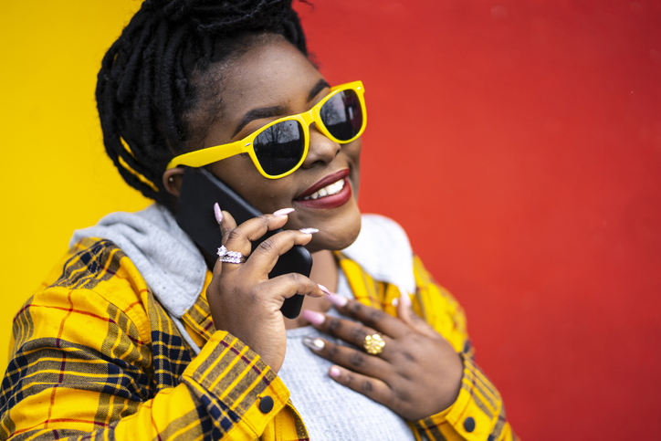 Young woman standing on colored background and talking on phone