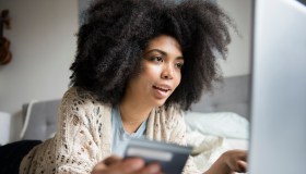 African American woman laying in bed online shopping with laptop