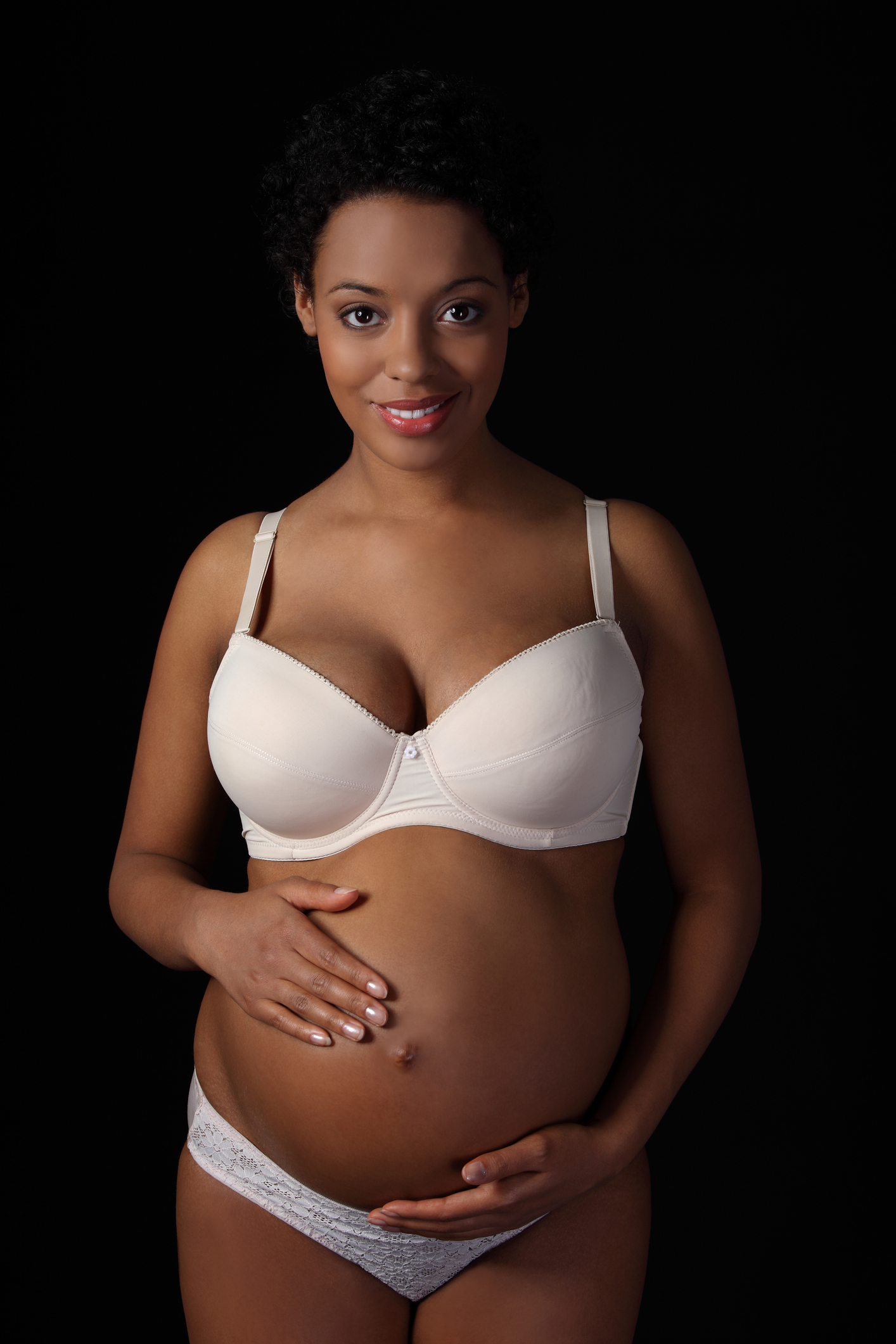 Portrait Of Smiling Young Woman Touching Abdomen While Standing Against Black Background