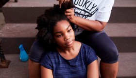 Black mother styling hair of daughter on staircase