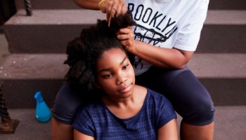 Black mother styling hair of daughter on staircase