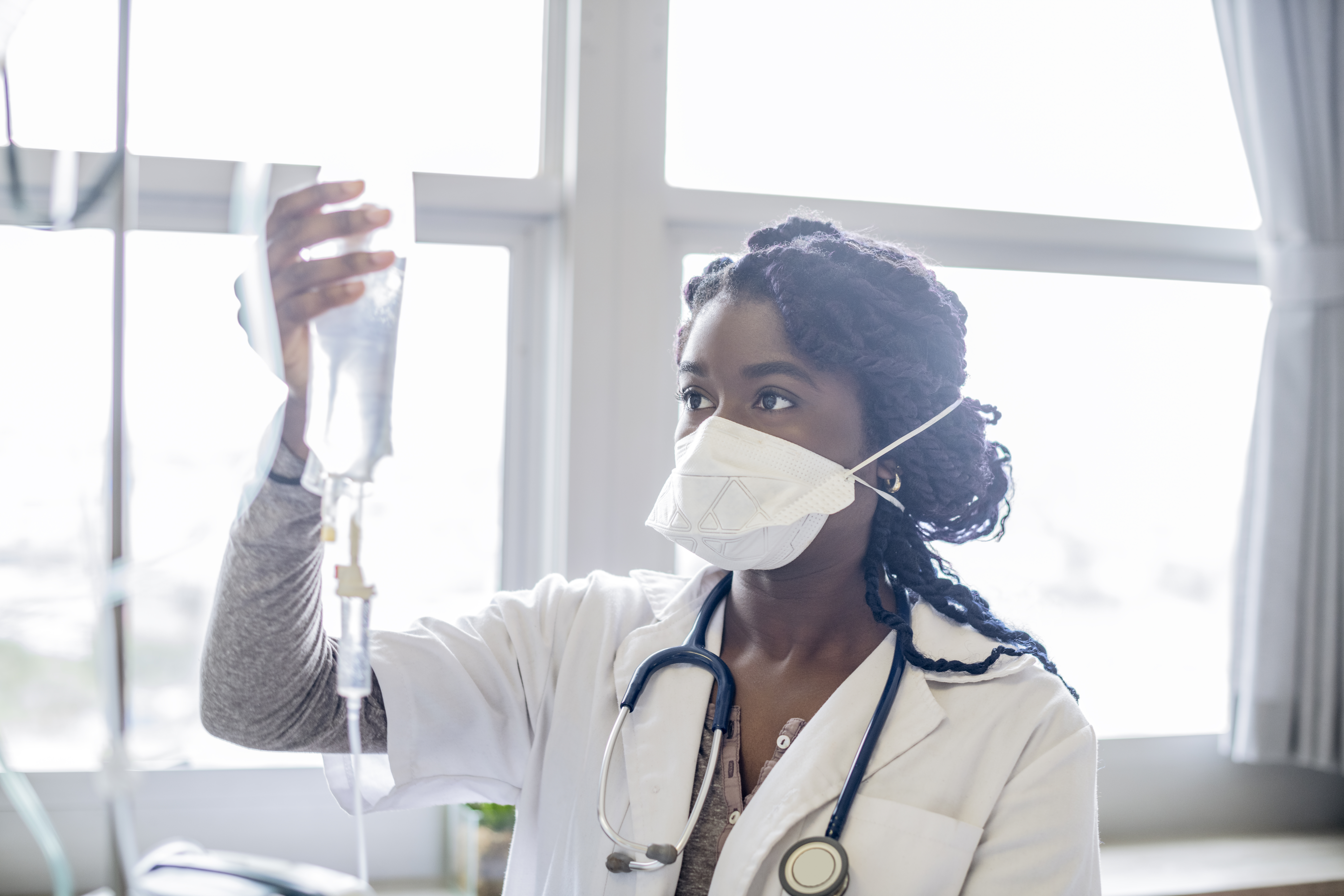 Young woman wearing face mask checking IV drip - stock photo