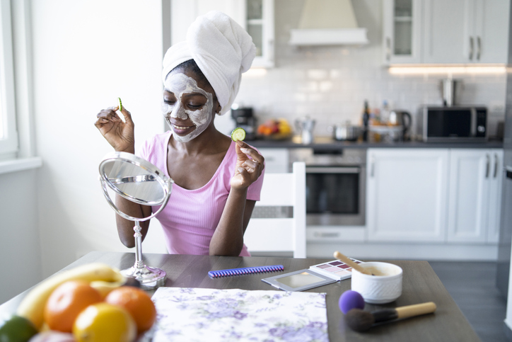 Smiling african woman with facial mask and towel on head, at home