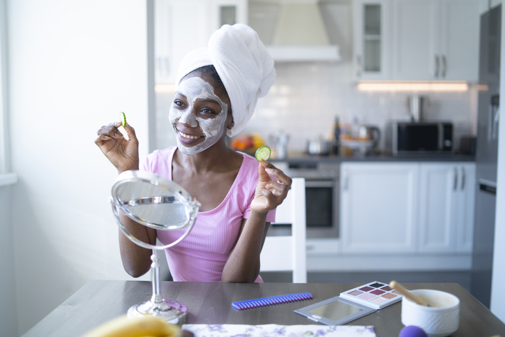 Smiling african woman with facial mask and towel on head, at home