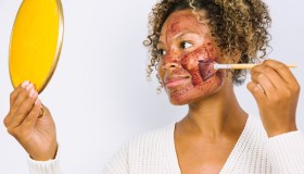 Woman Applying Face Mask Against White Background