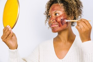 Woman Applying Face Mask Against White Background