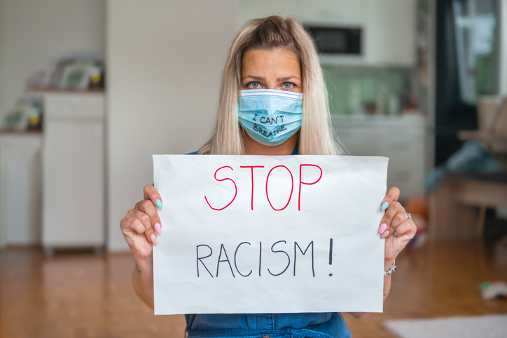 Young woman with face mask (I Can't Breathe) holding a poster with a message: STOP RACISM!