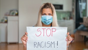 Young woman with face mask (I Can't Breathe) holding a poster with a message: STOP RACISM!