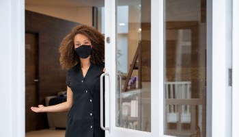 Business owner opening the door of her spa wearing a facemask