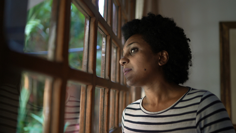 Mature women looking through window contemplating and thinking at home