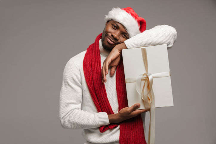 A young dark-skinned man in a woolen sweater, christmas hat and bright red scarf