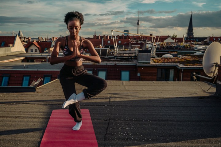 Young female standing on one leg while exercising on rooftop during sunrise