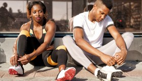 Athletes tying shoelaces while sitting on sidewalk at city