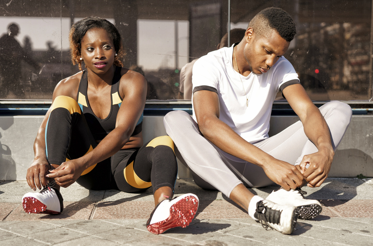Athletes tying shoelaces while sitting on sidewalk at city