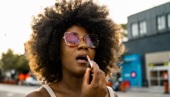 Young black woman on city street adjusting lipstick