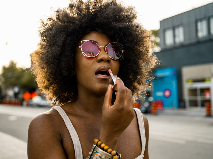 Young black woman on city street adjusting lipstick